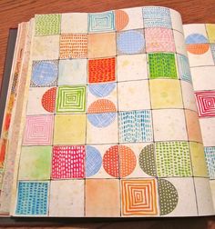 an open notebook with colorful squares and circles on it, sitting on top of a wooden table