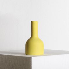 a yellow vase sitting on top of a white shelf in front of a white wall