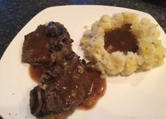 two pieces of meat, mashed potatoes and gravy on a white plate