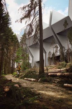 a man walking down a dirt road next to tall pine trees and a large building in the background