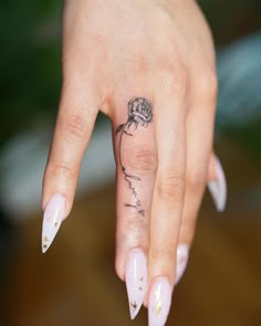 a woman's hand with a rose tattoo on her left thumb, and white fingernails