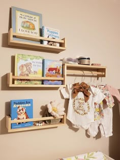 two wooden shelves holding books and baby's clothing hanging on the wall next to a crib