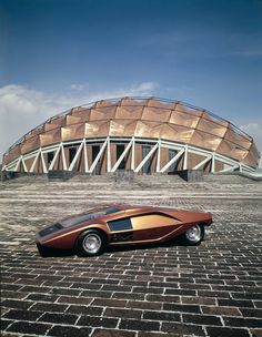 an unusual car is parked in front of a building with a domed structure behind it