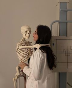 a woman standing next to a skeleton in a white lab coat looking at it's back