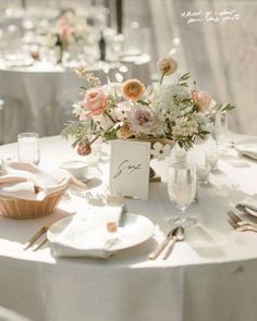 the table is set with white linens and silverware, flowers in vases