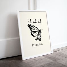 a white frame sitting on top of a wooden floor next to a wall with a black and white butterfly