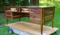 a wooden desk sitting on top of a piece of wood in front of some grass