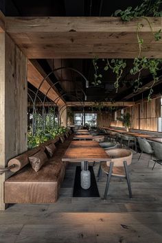 an empty restaurant with wooden benches and plants hanging from the ceiling, along with long tables