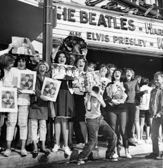 black and white photograph of people holding up pictures in front of the beatles theater sign