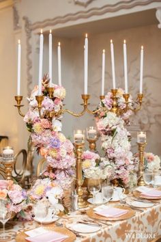 a table topped with lots of pink flowers and gold candelabra filled with candles