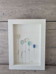 three blue and white balloons in a shadow box on a wooden surface with the words happy birthday written below them