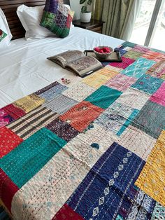 a bed with a colorful quilt on top of it next to two pillows and a book