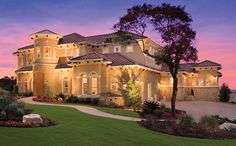 a large house with lots of windows and lights on it's front lawn at dusk