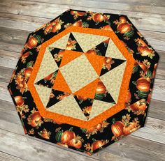 an orange and black quilted table topper with pumpkins in the center on a wooden surface