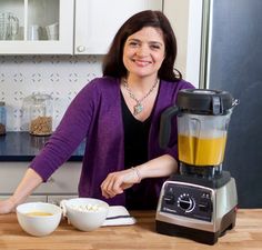 a woman standing next to a blender filled with food