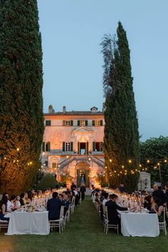 an outdoor dinner is set up in front of a large building with trees and lights