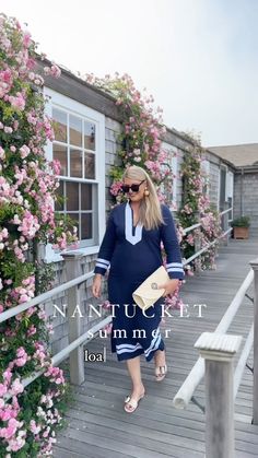 a woman walking down a wooden walkway next to pink flowers