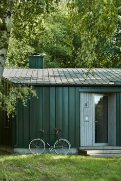 a bicycle is parked in front of a small green building with a door and windows