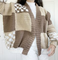 a woman wearing a brown and white crochet sweater holding her hand up in the air