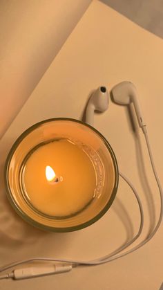 a glass bowl with a candle and headphones on it sitting next to a sheet of paper