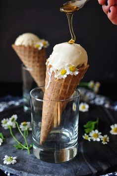 an ice cream cone is being drizzled with honey syrup and topped with daisies