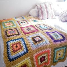 a crocheted blanket is on top of a bed with pillows and throw blankets