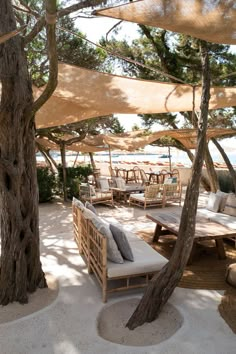 an outdoor seating area with tables and chairs under shade umbrellas on the sand beach