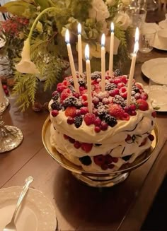 a cake with berries and candles on it sitting on top of a table next to plates