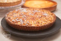 two pies sitting on top of black plates covered in powdered sugar next to each other