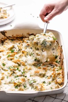 a casserole dish with chicken and cheese being lifted by a fork from the casserole