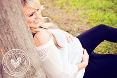 a beautiful blonde woman leaning against a tree