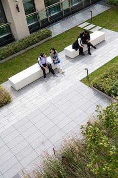 three people sitting on white benches in the middle of a courtyard with grass and bushes