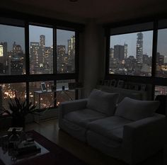 a living room filled with furniture and large windows overlooking the city lights at night time