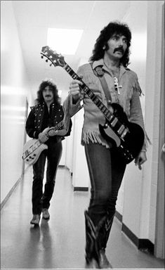 two people walking down a hallway with guitars in their hands and one person holding an electric guitar