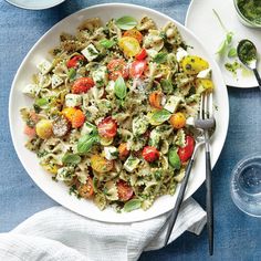 a white plate topped with pasta salad next to two bowls of pesto and tomatoes