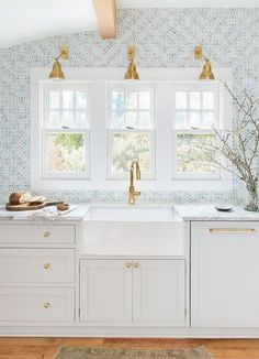 a kitchen with white cabinets and gold faucets in the window sill,