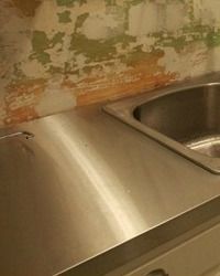 a stainless steel sink and counter in a room with peeling paint on the wall behind it