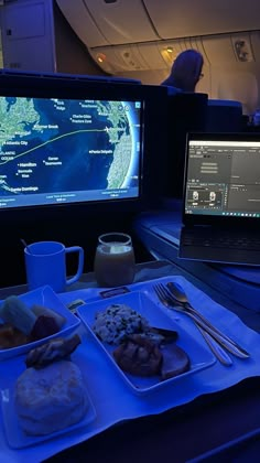 a laptop computer sitting on top of a desk next to a tray with food and drinks