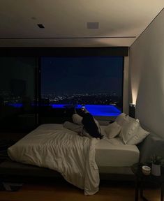 a dog sitting on top of a bed in a room with large windows overlooking the city