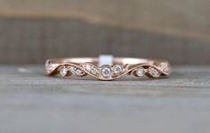 a rose gold wedding band with diamonds on it's side, sitting on a wooden surface