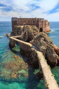 an old castle on the edge of a cliff by the ocean with clear blue water