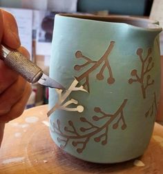 a person is using a sharp knife to cut out leaves on a cup that has been painted