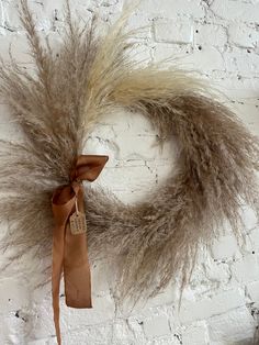 a dried wreath on a brick wall with a brown ribbon hanging from it's center