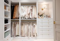 the closet is full of white clothes and gold hardware on the doors, along with other items