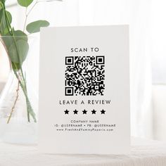 a card with a qr code on it sitting next to a vase filled with flowers