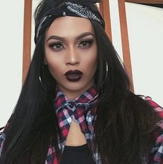 a woman with long black hair wearing a bandana and dark lipstick looks at the camera