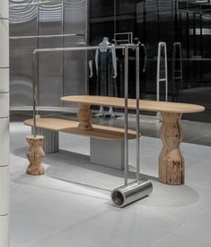 a bench and two stools in front of a glass wall with clothes hanging on it