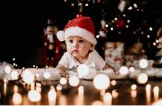 a baby wearing a santa hat sitting in front of some christmas lights on the ground