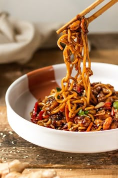 someone is eating noodles with chopsticks in a white bowl on a wooden table