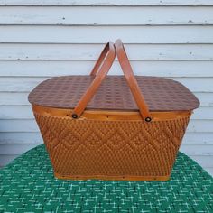 a brown wicker basket sitting on top of a green cloth covered table next to a white house